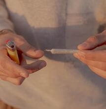 a young person holding a pre-rolled joint and a lighter in their hands. 