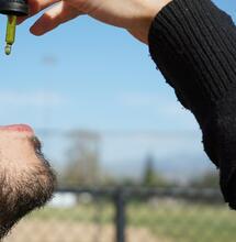 a man is taking a drop of CBD oil, which is available as full-spectrum, broad-spectrum and isolate form 