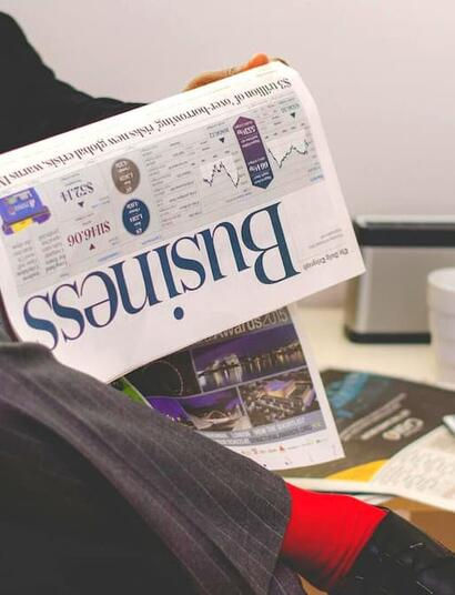 Business professional reading a financial newspaper with stock market charts and reports, symbolizing investment analysis and market trends.