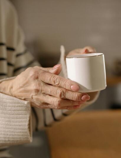 Primer plano de las manos de una persona mayor sosteniendo una taza con firmeza, ilustrando la búsqueda de control motor y reducción de temblores en el Parkinson con cannabis medicinal.