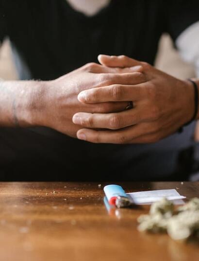 Person sitting with hands clasped at a table, cannabis buds and a lighter placed in the foreground, symbolizing a cannabis tolerance break and mindful pause from consumption.