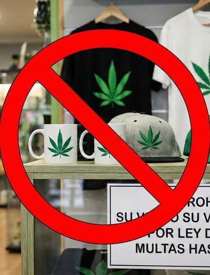 Interior de un grow shop con una señal de prohibido roja sobre productos de merchandising (camisetas, tazas, gorras) con la hoja de marihuana. Un cartel advierte de la prohibición de venta y regalo por la Ley de Galicia con multas de hasta 600.000€.