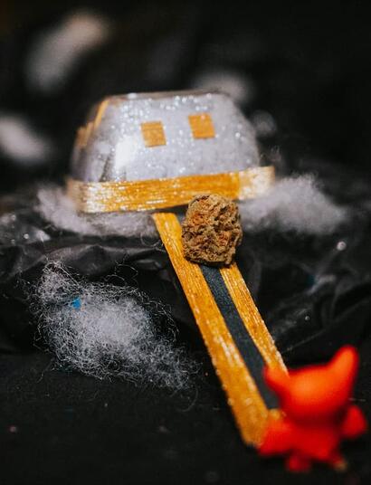 A small toy with smiley face is placed on top of a rock and there is a green-yellow bud of cannabis at the center of the toy. 