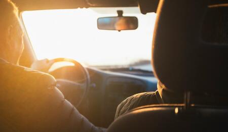 Un primer plano enfocado en el interior de un coche moderno a última hora de la tarde, mostrando las manos de un conductor agarrando el volante.