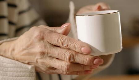 Primer plano de las manos de una persona mayor sosteniendo una taza con firmeza, ilustrando la búsqueda de control motor y reducción de temblores en el Parkinson con cannabis medicinal.