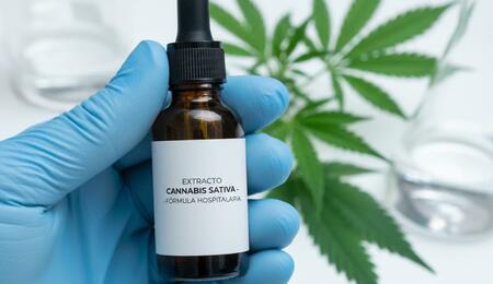 Un profesional sanitario con guante sostiene un frasco con gotero de aceite de cannabis medicinal, representando la nueva regulación en España.