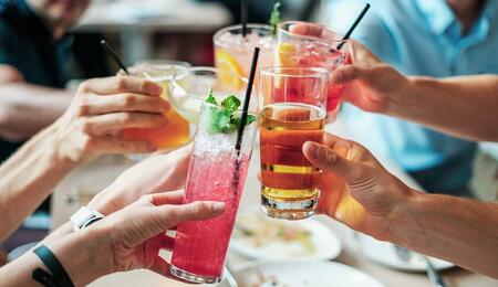 a group of people cheering up with alcoholic drinks over a holiday table. 