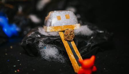 A small toy with smiley face is placed on top of a rock and there is a green-yellow bud of cannabis at the center of the toy.