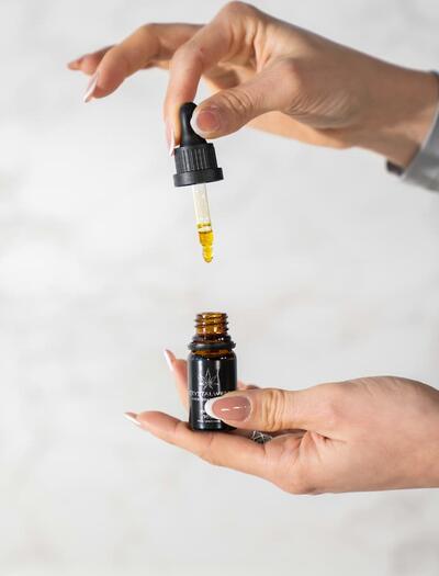 Una mano profesional sostiene un cuentagotas con aceite de CBD sobre un frasco de vidrio en un entorno de iluminación clara y aséptica. La imagen simboliza la dosificación precisa y el rigor clínico en el tratamiento de la epilepsia genética.