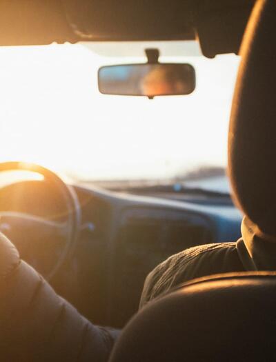 Un primer plano enfocado en el interior de un coche moderno a última hora de la tarde, mostrando las manos de un conductor agarrando el volante.
