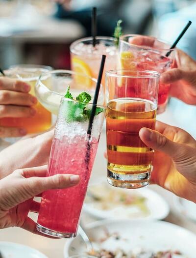 a group of people cheering up with alcoholic drinks over a holiday table. 