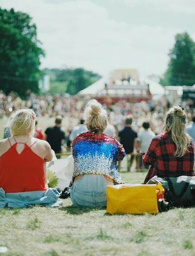 Festival attendees relax on a grassy field under the summer sun while watching performances from a distance at an outdoor music festival.