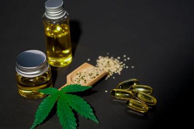 Glass bottles of CBD oil, softgel capsules, hemp seeds, and a cannabis leaf arranged on a dark surface, illustrating hemp-derived CBD products used to support wellness and post-exercise recovery.