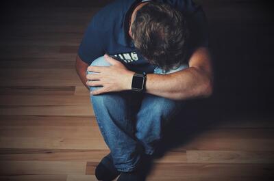 Person sitting on the floor with head down and arms wrapped around their knees, symbolizing depression, emotional stress, or low mood.