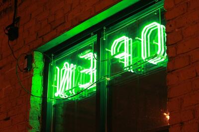 A green neon sign that says “Open” on the window of a local cannabis lounge area where users can socialize. 