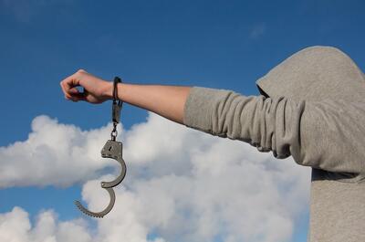 a young man with a handcuff hanging from his hand against a blue sky symbolizing freedom.