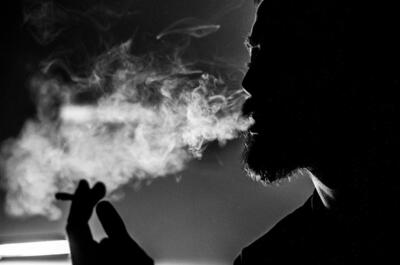 A black-and-white silhouette of a person exhaling cannabis smoke indoors.