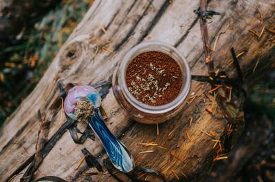 Glass jar of ground cannabis and a colorful glass pipe resting on a wooden surface outdoors.