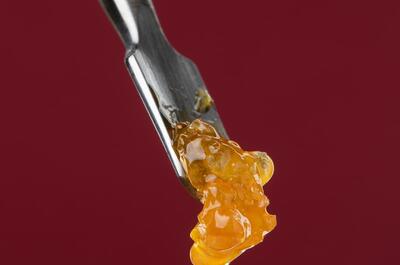 illustrative rosin photo of a yellow sticky and bubbly substance on a dabber against a dark red background.