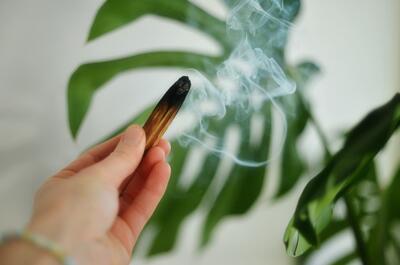 A person holding a pre-roll as secondhand smoke fills the room, with a blurred green cannabis flower visible in the background.