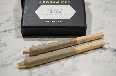a black box with branded artisan delta-8 cannabis pre-rolls along with two mini joints on a white surface.