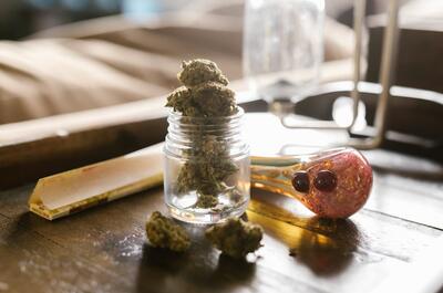 a photo showing cannabis accessories for smoking such as glass pipe and rolling papers, and a jar filled with weed buds. 