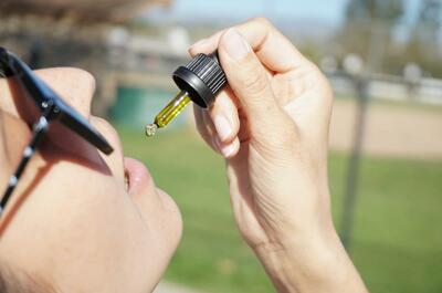 Person using a dropper to place CBD oil under the tongue outdoors, demonstrating sublingual administration of cannabidiol.