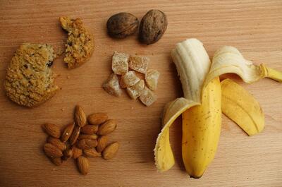 healthy foods such as diet cookie, almonds, peeled banana, chestnuts and dried fruit laid on a table.